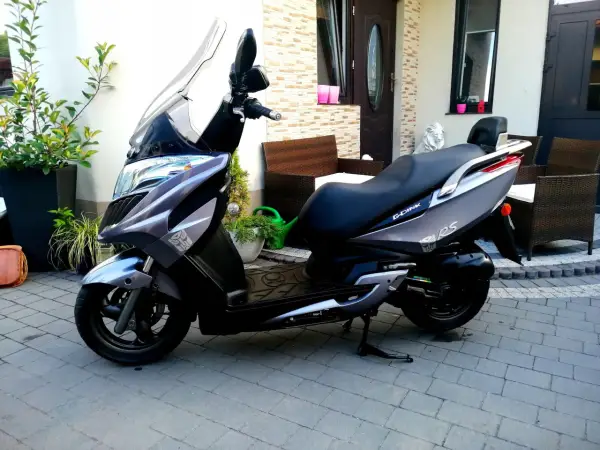 Elegancki skuter Kymco Dink 50 w kolorze grafitowym stoi na podjeździe, gotowy do jazdy.