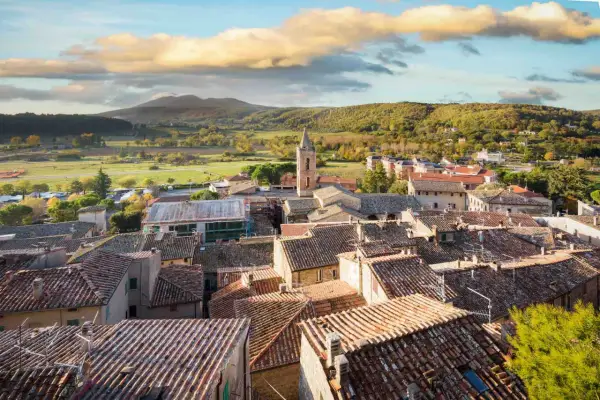 Panoramica di Sarteano cosa vedere: tetti in cotto, campanile e colline verdi sotto un cielo nuvoloso.