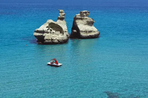 Due faraglioni bianchi emergono dal mare cristallino, con una pedalò che naviga vicino alla spiaggia dell'orso.