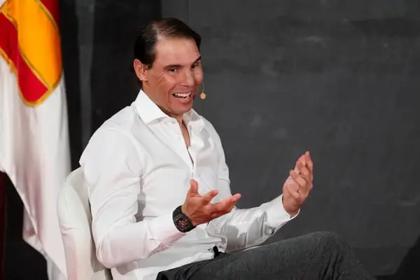 Rafael Nadal, znany z imponującego majątku, w białej koszuli, z uśmiechem i gestykulując.