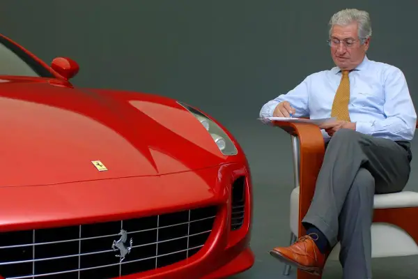 Un uomo d'affari con una cravatta gialla scrive appunti accanto a una Ferrari rossa, forse per le recensioni del film.