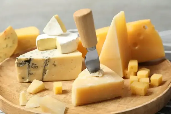 Deska serów: pleśniowy, camembert i twarde sery, w tym ser sałatkowy pokrojony w kostkę.