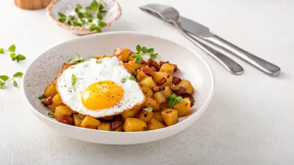 Un œuf au plat sur des pommes de terre sautées avec des lardons, une idée parfaite avec quoi accompagner des œufs pour un repas savoureux.