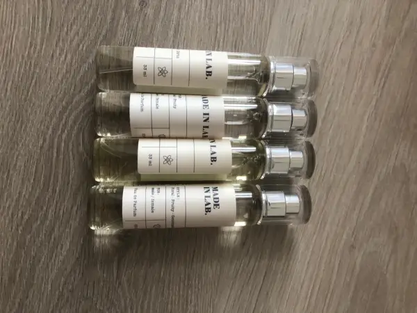 Cztery małe flakoniki perfum "MADE IN LAB." na drewnianym tle. Opinie o nich są pozytywne, doceniane za zapachy.