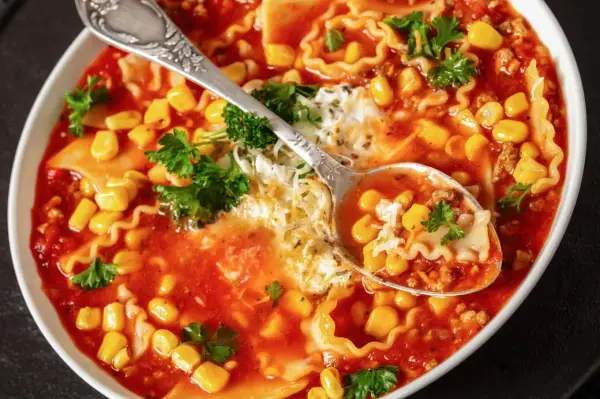 Herzhafte Lasagne Suppe mit Mais, Hackfleisch und Nudeln, garniert mit Petersilie und Käse. Eine Löffelprobe zeigt die köstlichen Zutaten.