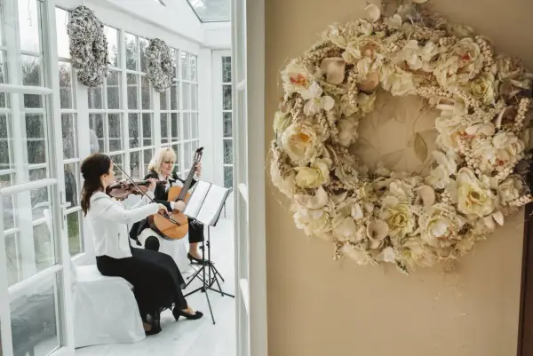 Dwie artystki grają na skrzypcach i gitarze, tworząc oprawę muzyczną ślubu. Cena takiej usługi zależy od wielu czynników.