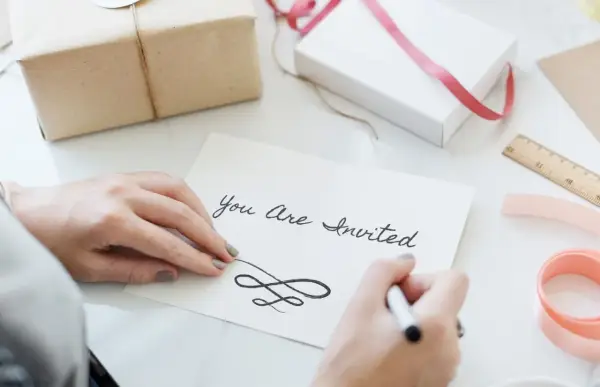 Ręce piszą zaproszenie "You Are Invited". Dowiedz się, jak napisać zaproszenie na urodziny po angielsku.