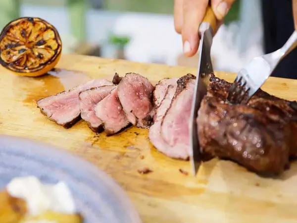 Perfekt grillad ryggbiff skärs upp på en skärbräda. Bredvid ligger en grillad citronhalva.