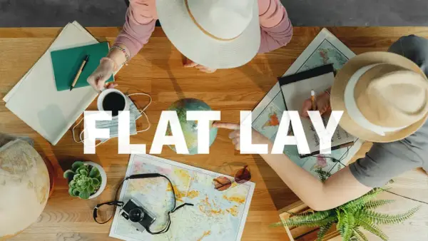 Widok z góry na stół z mapami, globusem, aparatem, notatnikiem i kawą. Dwie osoby planują podróż, tworząc idealny **flat lay**.