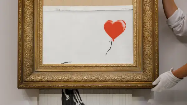 A framed Banksy artwork featuring a red balloon, hinting at how is Banksy rich.