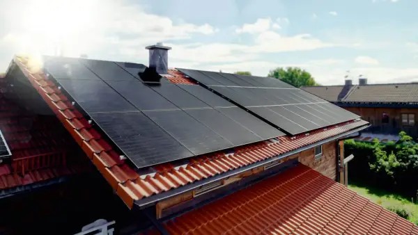 Solceller monterade på ett tegeltak. Solen skiner och fångas upp av panelerna.