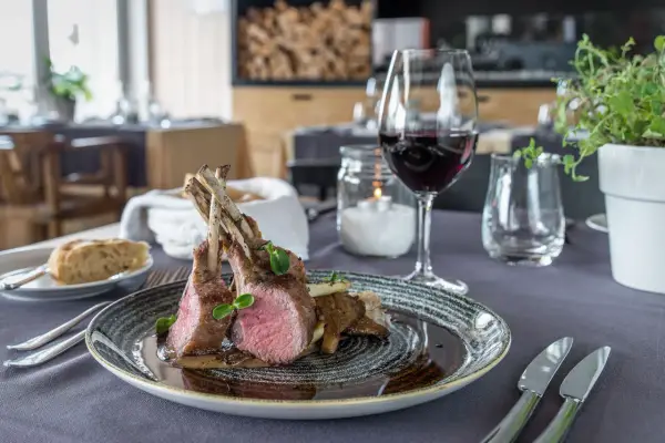Carré d'agnello al forno con funghi e un bicchiere di vino rosso, un abbinamento perfetto per un pasto speciale.