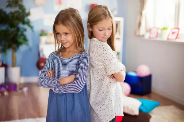 Dwie dziewczynki stoją plecami do siebie ze skrzyżowanymi rękami. W tle pokój dziecięcy. Jak nie zwariować ze swoim dzieckiem?