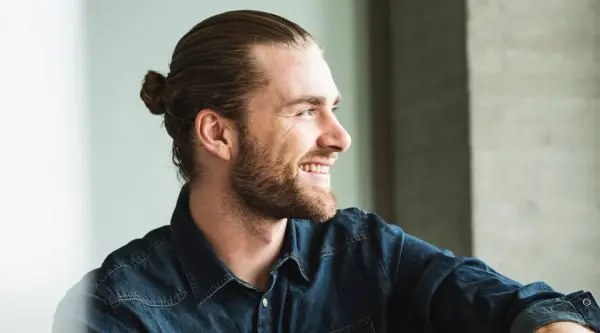 Lächelnder Mann mit Bart und einem lässigen **man bun** im Jeanshemd.