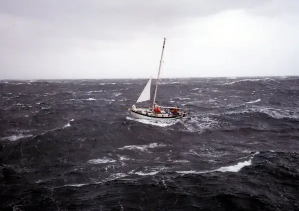 Un voilier affronte une mer agitée, sa voile blanche tendue. La mise à la cape est une manœuvre de survie face aux éléments déchaînés.