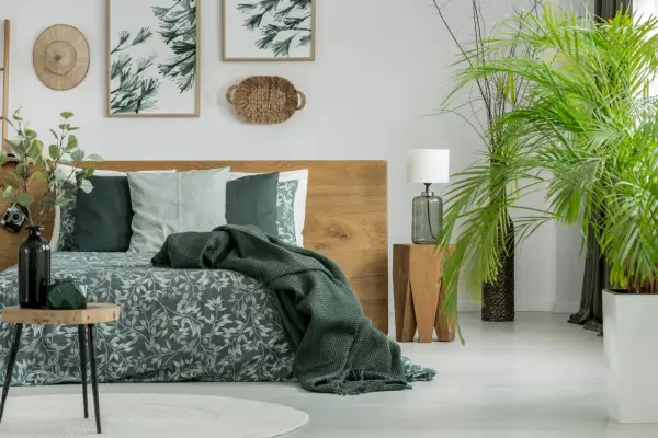 Sypialnia w stylu boho z drewnianym łóżkiem i pościelą w liście. Kolor khaki z czym łączyć? Z zielenią roślin i naturalnymi materiałami.