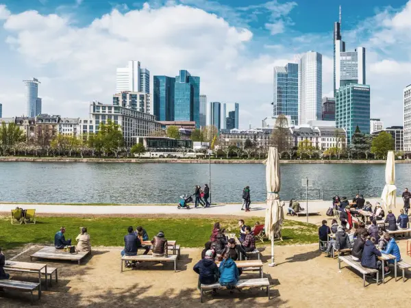Frankfurt Geheimtipps: Menschen genießen das Leben am Mainufer mit Blick auf die Skyline. Ein perfekter Ort zum Entspannen und Beobachten.