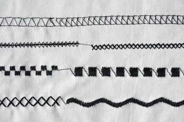 Close-up of various black sewing machine stitches on white fabric.