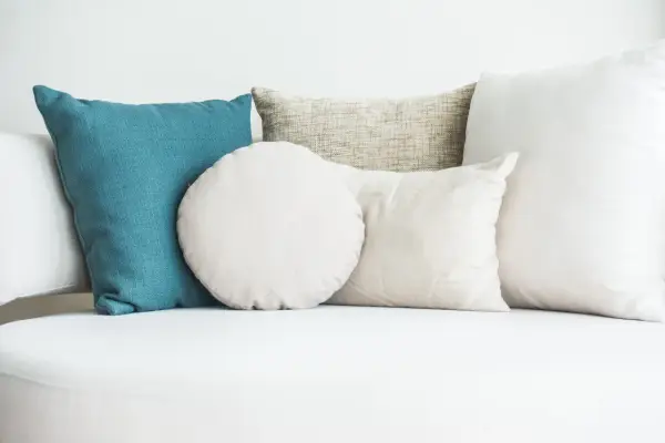 Cuscini di varie forme e colori su un divano bianco. Scopri come lavare i cuscini del divano per mantenerli freschi e puliti.
