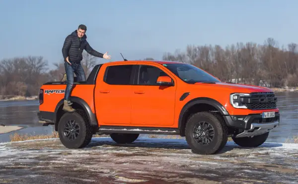 Pomarańczowy Ford Ranger Raptor z kierowcą na pace, gotowy na zimową przygodę nad rzeką.
