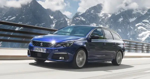 Niebieski Peugeot 308 T9 kombi jedzie po górskiej drodze, z ośnieżonymi szczytami w tle.