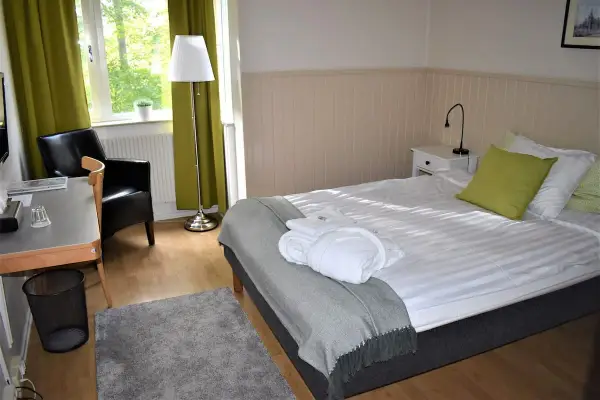 Ett mysigt rum på Wendelsbergs Hotell & Vandrarhem med en bekväm säng, fåtölj och skrivbord.