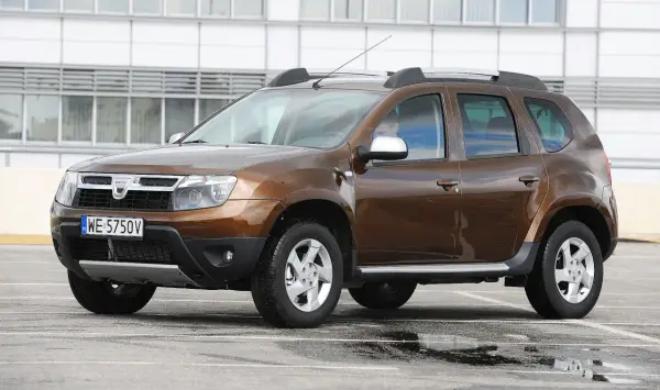Brązowy Dacia Duster na parkingu. Zastanawiasz się, dacia duster jaki silnik wybrać? Ten model ma napęd 4x4.