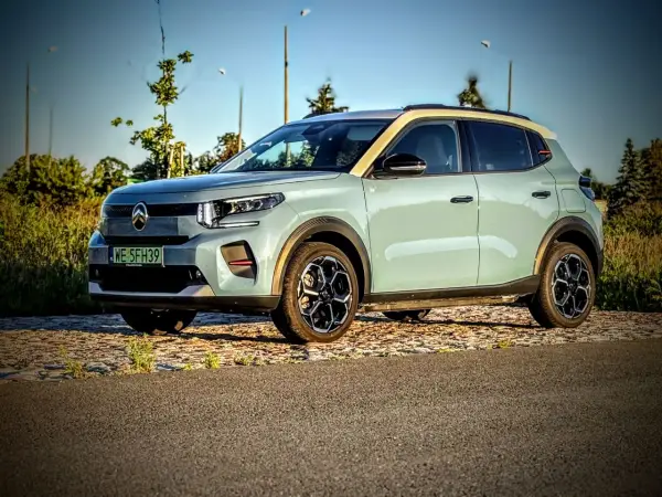 Jasnoszary Citroën ë-C3 z żółtym dachem stoi na tle drzew i nieba.