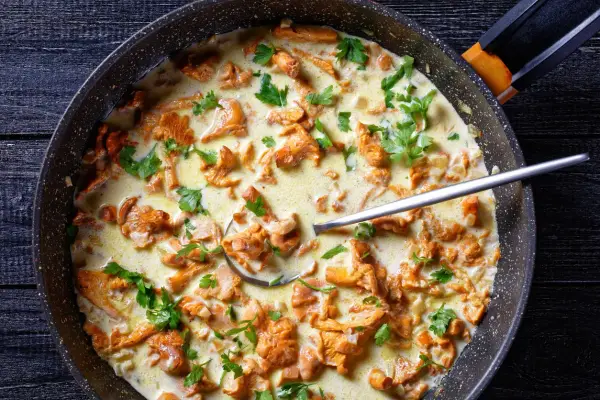 Pfifferlinge in cremiger Rahmsauce, garniert mit frischer Petersilie, in einer Pfanne. Ein Löffel ragt aus der köstlichen Speise.