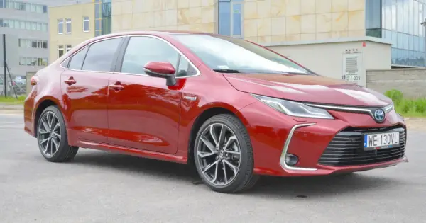 Błyszcząca, czerwona Toyota Corolla 1.8 Hybrid stoi na tle nowoczesnego budynku.