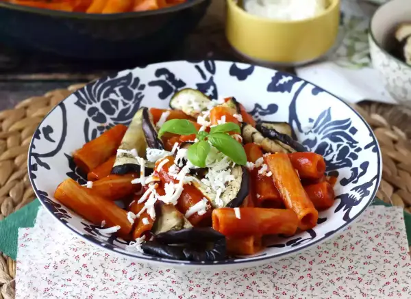 Pâtes rigatoni généreusement garnies de sauce tomate, d'aubergines grillées et de fromage râpé, le tout surmonté d'une feuille de basilic frais. Un plat de pâtes aubergines appétissant.