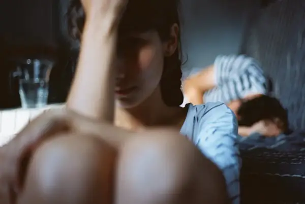 Une femme au premier plan, le visage caché, semble accablée. Au fond, une autre personne se recroqueville. L'image évoque la **dépression et la libido** affectées par le mal-être.