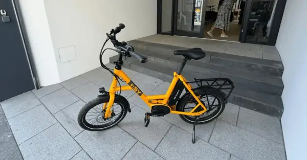 Gelbes i:SY E-Bike, das bei der Stiftung Warentest gut abgeschnitten hat, steht auf gepflastertem Untergrund vor einer Treppe.