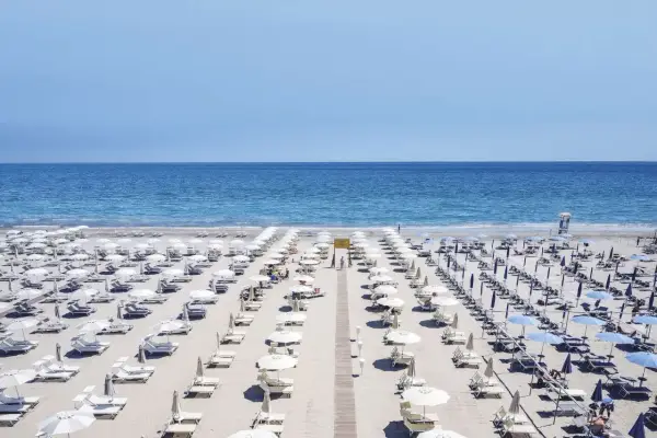 File di ombrelloni bianchi e lettini ordinati sui **stabilimenti balneari Cervia**, con il mare azzurro sullo sfondo.