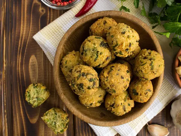 Schüssel mit frittierten Falafel-Bällchen, die aus frischen falafel zutaten zubereitet wurden. Daneben liegen Knoblauch und Kräuter.