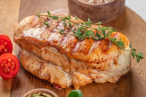 Soczysty filet z indyka, pieczony z ziołami, podany z pomidorkami koktajlowymi na drewnianej desce.