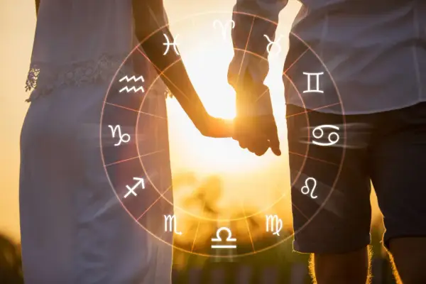 Para, trzymająca się za ręce, na tle zachodzącego słońca, z widocznym kołem zodiaku, gdzie widnieją symbole byka i koziorożca.