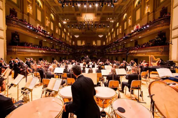 Un orchestre symphonique interprète de la musique classique moderne dans une salle de concert ornée, avec des musiciens jouant de divers instruments.