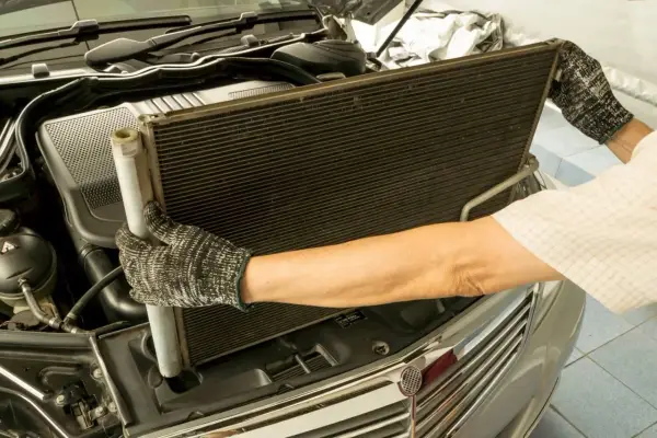 Mechanik w rękawicach wyjmuje skraplacz klimatyzacji z samochodu.