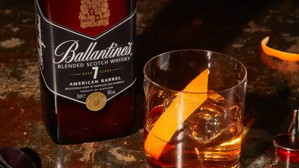 Orzeźwiający drink: whisky z wodą gazowaną, lodem i skórką pomarańczy, obok butelka Ballantine's.