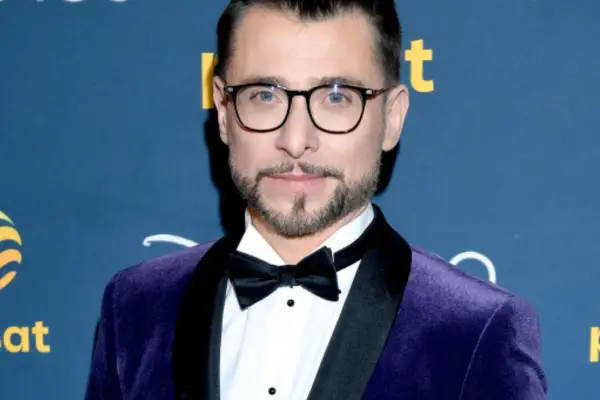 Kacper Kuszewski w fioletowym aksamitnym garniturze z czarną muszką. Wygląda elegancko, jakby wybierał się na galę z żoną.