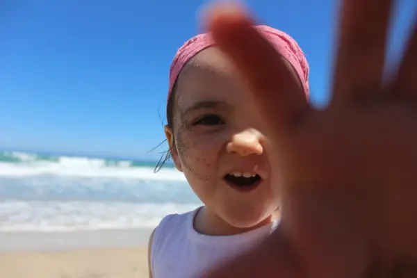 Niña con bandana rosa y arena en la cara, disfrutando de sus viajes con niños en la playa.