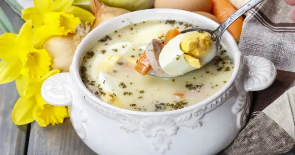 Aromaticzny żur z jajkiem i kiełbasą, podany w ozdobnej misce, z żółtymi narcyzami w tle.