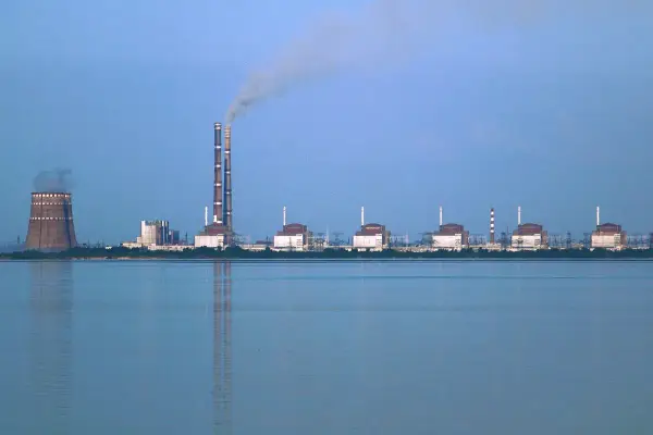 Zaporoże: potężna elektrownia atomowa z chłodnią kominową i dymiącymi kominami, na tle spokojnej wody.