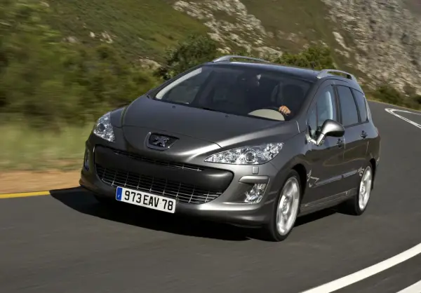 Szary Peugeot 308 2008 na krętej drodze wśród zielonych wzgórz.