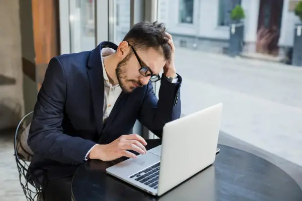 Zestresowany mężczyzna w garniturze pracuje przy laptopie, próbując skrócenie pauzy do 7 godzin.