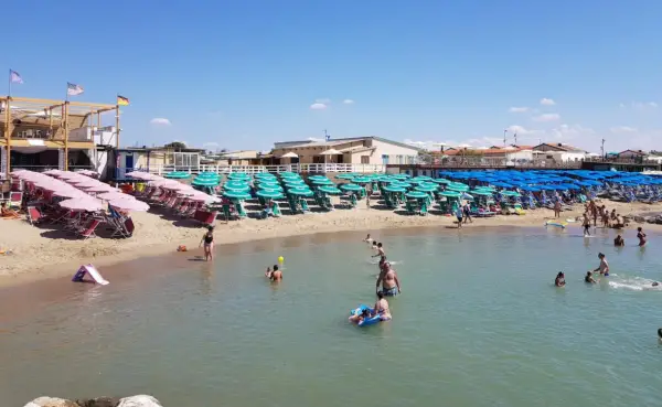 Plage de Marina di Pisa animée, avec des rangées de parasols et de chaises longues sur le sable, et des baigneurs profitant de l'eau claire sous un ciel bleu.