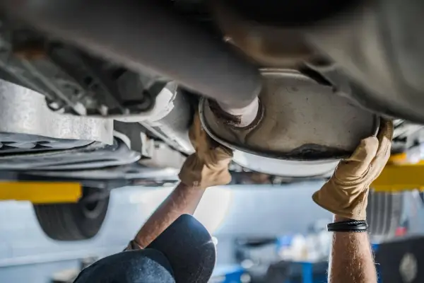 Mani guantate lavorano sul sistema di scarico, forse sostituendo il catalizzatore auto.