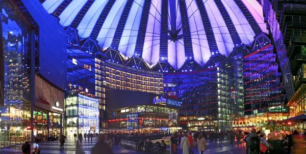 Nocny widok na Sony Center w Berlinie, z oświetlonym dachem i fasadami budynków, pełen ludzi spacerujących po placu.