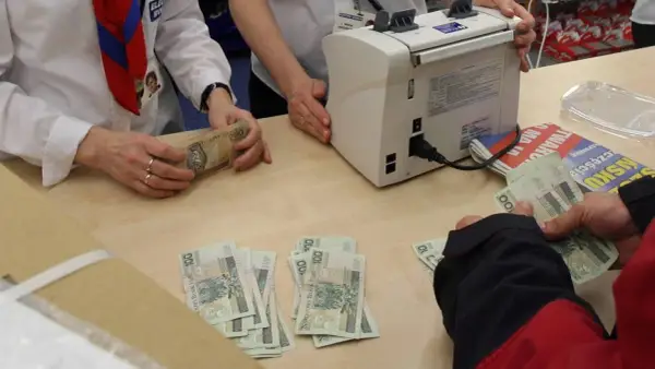 Ręce liczą banknoty 100 i 200 zł. Obok maszyna do liczenia pieniędzy. W tle gazety. Płatność gotówką do jakiej kwoty jest dozwolona?